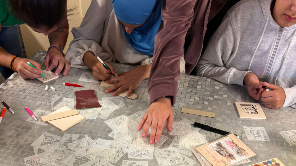 Ragazzi del Centro Socio Educativo Tandem partecipano a un laboratorio creativo, decorando piccoli oggetti artigianali attorno a un tavolo.