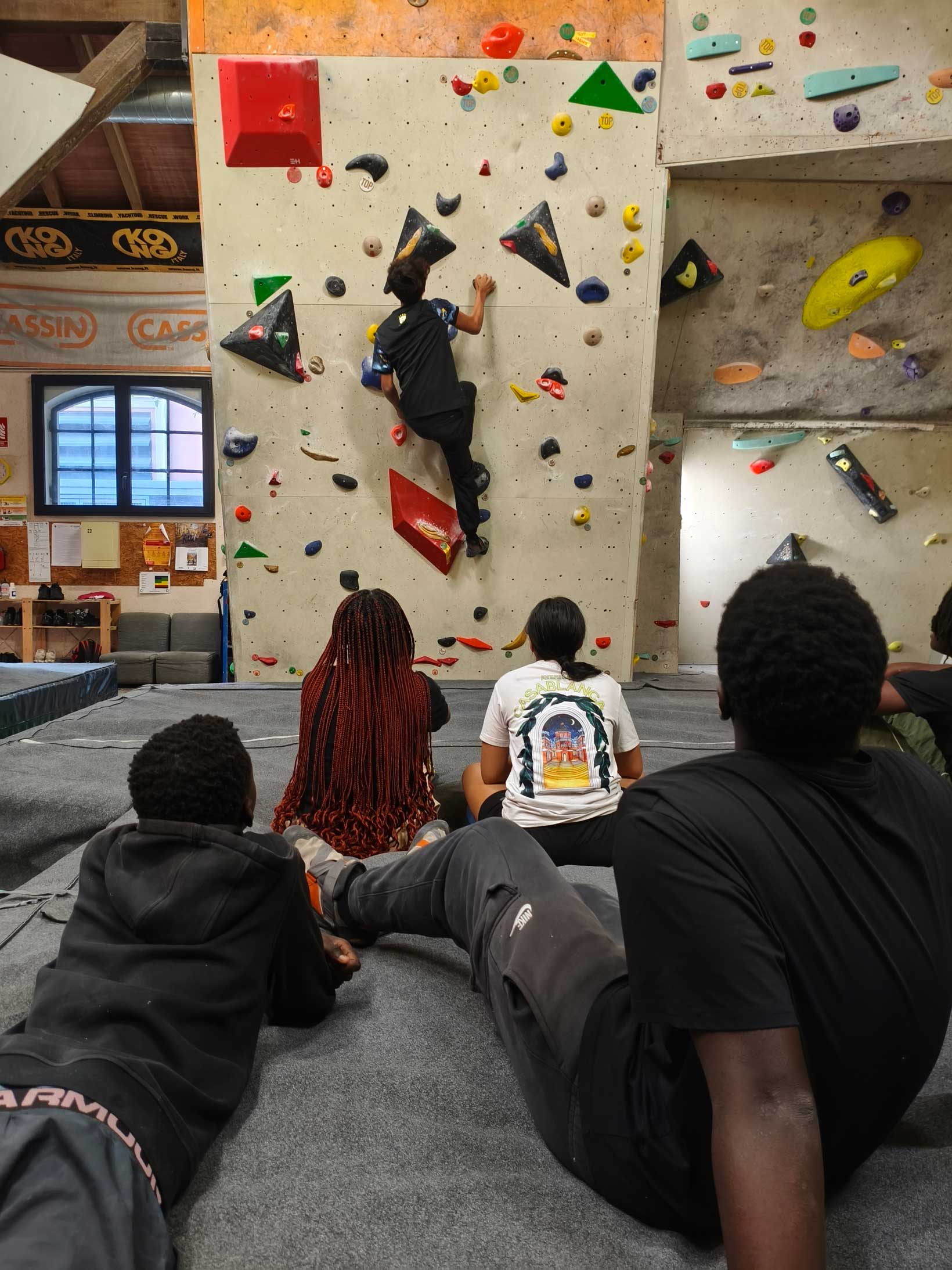 Ragazzi del Centro Socio Educativo Tandem partecipano a un laboratorio di arrampicata, osservando un compagno sulla parete.