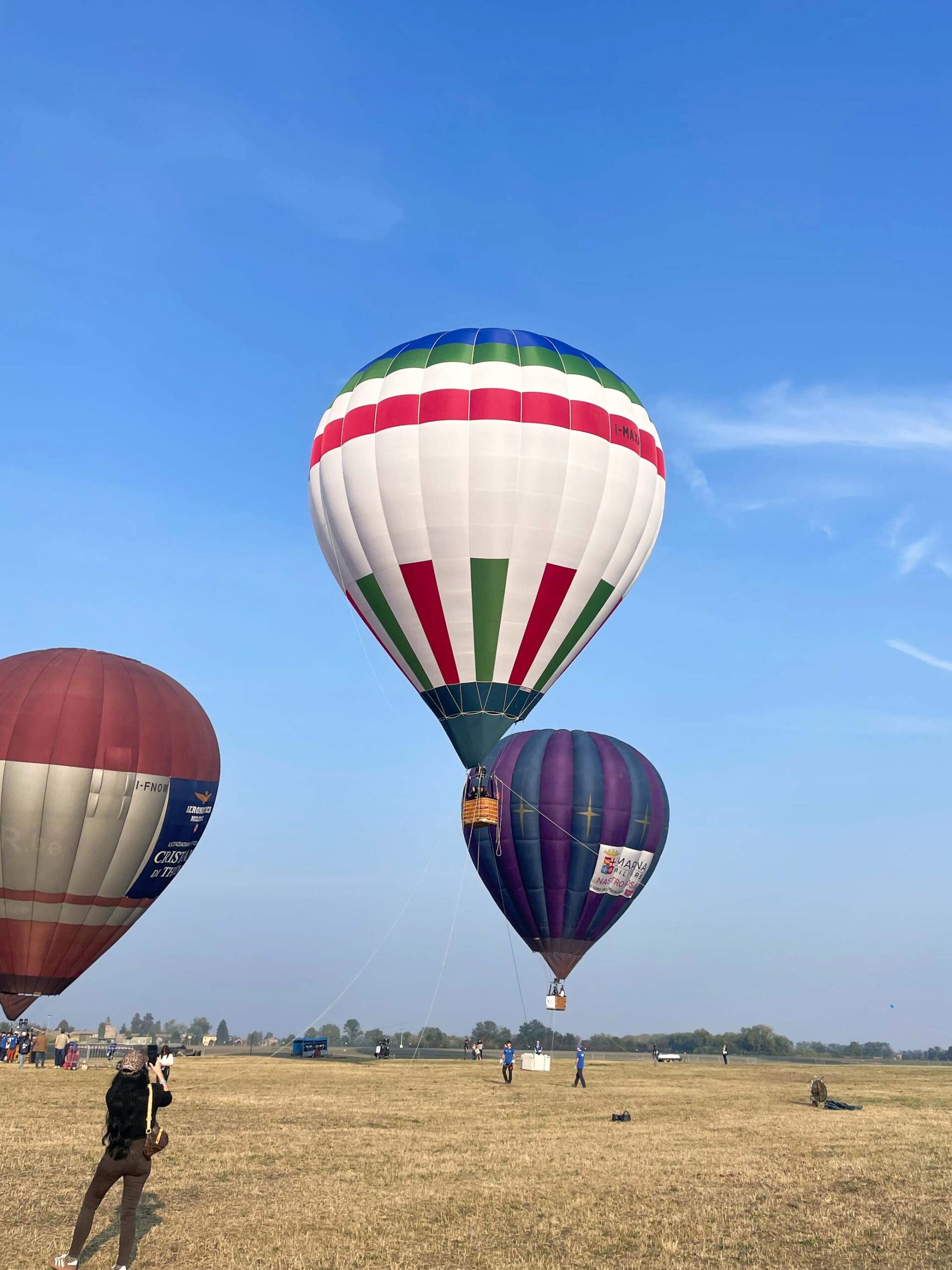 Mongolfiere colorate alla Balloon CUP nell’area dell’Aeroporto Militare di San Damiano, mentre una persona le fotografa dal campo.